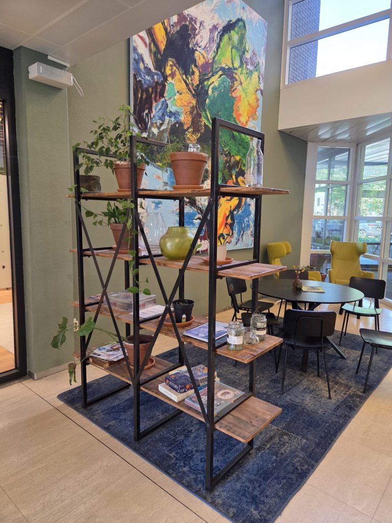 Moderne open ruimte met boekenrek, planten en kleurrijke wandkunst.