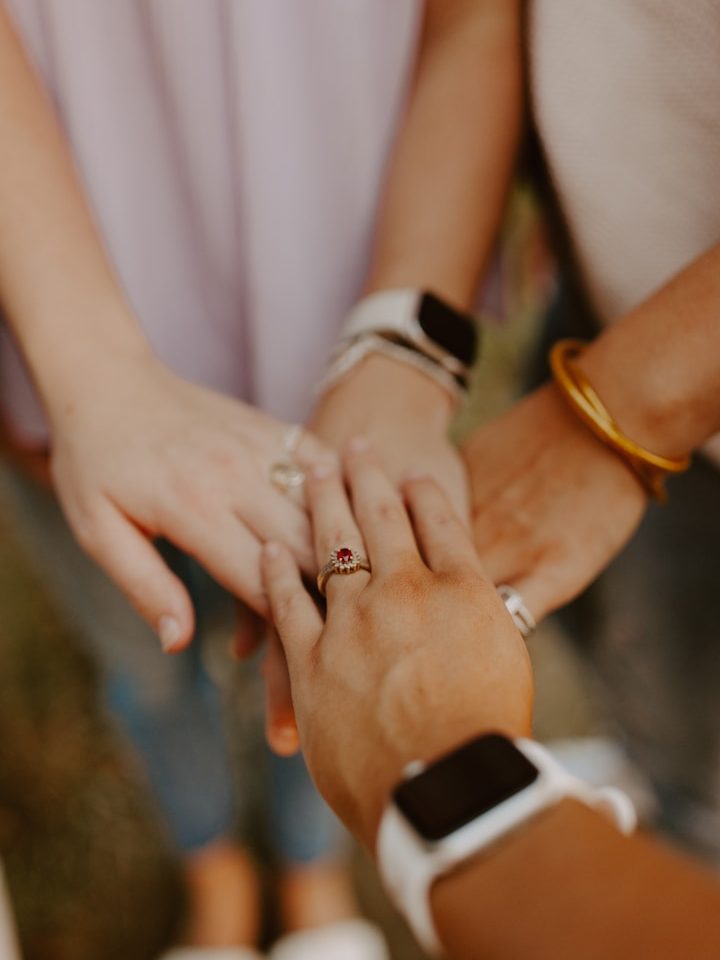Vijf handen op elkaar gestapeld, enkele met ringen en horloges.